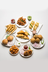Indian Tea time snacks  in group includes Veg Samosa, Kachori/kachaudi, aloo bonda, khaman dhokla, bread, onion,chilli and moong pakora/pakoda/bhaji/bhajji/Bhajiya/bajji with sauces, selective focus