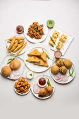 Indian Tea time snacks  in group includes Veg Samosa, Kachori/kachaudi, aloo bonda, khaman dhokla, bread, onion,chilli and moong pakora/pakoda/bhaji/bhajji/Bhajiya/bajji with sauces, selective focus