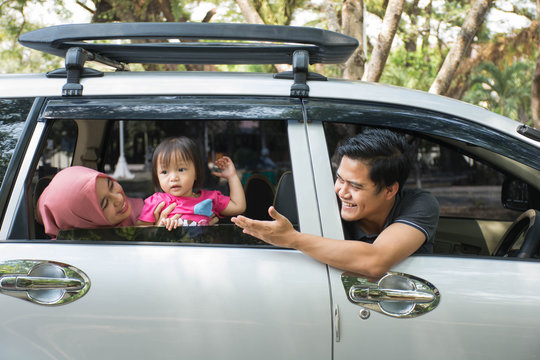 Young Muslim Family , Transport, Leisure, Road Trip And People Concept - Side View Of Happy Man, Woman And Little Girl  Ready For Traveling Inside A Car Looking Out Windows At Sunny Day