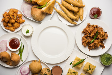 Indian Tea time snacks  in group includes Veg Samosa, Kachori/kachaudi, aloo bonda, khaman dhokla, bread, onion,chilli and moong pakora/pakoda/bhaji/bhajji/Bhajiya/bajji with sauces, selective focus