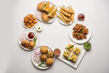 Indian Tea time snacks  in group includes Veg Samosa, Kachori/kachaudi, aloo bonda, khaman dhokla, bread, onion,chilli and moong pakora/pakoda/bhaji/bhajji/Bhajiya/bajji with sauces, selective focus