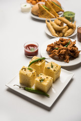 Indian Tea time snacks  in group includes Veg Samosa, Kachori/kachaudi, aloo bonda, khaman dhokla, bread, onion,chilli and moong pakora/pakoda/bhaji/bhajji/Bhajiya/bajji with sauces, selective focus