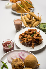 Indian Tea time snacks  in group includes Veg Samosa, Kachori/kachaudi, aloo bonda, khaman dhokla, bread, onion,chilli and moong pakora/pakoda/bhaji/bhajji/Bhajiya/bajji with sauces, selective focus