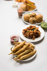 Indian Tea time snacks  in group includes Veg Samosa, Kachori/kachaudi, aloo bonda, khaman dhokla, bread, onion,chilli and moong pakora/pakoda/bhaji/bhajji/Bhajiya/bajji with sauces, selective focus