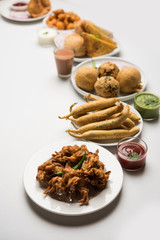 Indian Tea time snacks  in group includes Veg Samosa, Kachori/kachaudi, aloo bonda, khaman dhokla, bread, onion,chilli and moong pakora/pakoda/bhaji/bhajji/Bhajiya/bajji with sauces, selective focus