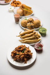 Indian Tea time snacks  in group includes Veg Samosa, Kachori/kachaudi, aloo bonda, khaman dhokla, bread, onion,chilli and moong pakora/pakoda/bhaji/bhajji/Bhajiya/bajji with sauces, selective focus