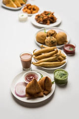 Indian Tea time snacks  in group includes Veg Samosa, Kachori/kachaudi, aloo bonda, khaman dhokla, bread, onion,chilli and moong pakora/pakoda/bhaji/bhajji/Bhajiya/bajji with sauces, selective focus