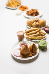 Indian Tea time snacks  in group includes Veg Samosa, Kachori/kachaudi, aloo bonda, khaman dhokla, bread, onion,chilli and moong pakora/pakoda/bhaji/bhajji/Bhajiya/bajji with sauces, selective focus