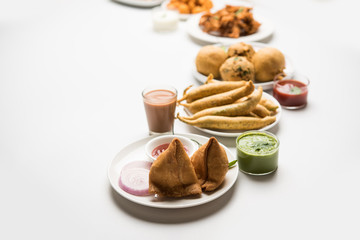 Indian Tea time snacks  in group includes Veg Samosa, Kachori/kachaudi, aloo bonda, khaman dhokla, bread, onion,chilli and moong pakora/pakoda/bhaji/bhajji/Bhajiya/bajji with sauces, selective focus