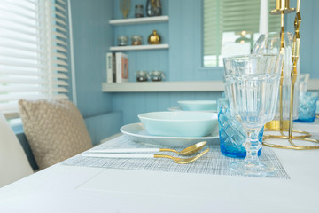 Pale blue plate setting on table with gold candle holder in home dining room interior. 