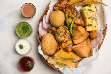 Indian Tea time snacks  in group includes Veg Samosa, Kachori/kachaudi, aloo bonda, khaman dhokla, bread, onion,chilli and moong pakora/pakoda/bhaji/bhajji/Bhajiya/bajji with sauces, selective focus