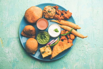 Indian Tea time snacks  in group includes Veg Samosa, Kachori/kachaudi, aloo bonda, khaman dhokla, bread, onion,chilli and moong pakora/pakoda/bhaji/bhajji/Bhajiya/bajji with sauces, selective focus
