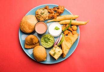 Indian Tea time snacks  in group includes Veg Samosa, Kachori/kachaudi, aloo bonda, khaman dhokla, bread, onion,chilli and moong pakora/pakoda/bhaji/bhajji/Bhajiya/bajji with sauces, selective focus