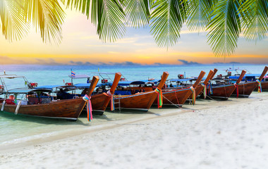Wooden boats parking at the white beach on tropical sea with twilight sky and sunlight , and have green palm leafs on top.