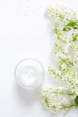 Flat lay composition with Moisturizing face cream and beautiful white  flowers on white background.Skin care cosmetics. Beauty blogger concept. Moisturizer natural hygiene product with flowers. 
