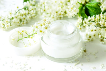 Fototapeta na wymiar Face and body cream. Jar of body cream and beautiful white flowers on white background. Close-up. Healthcare concept. Moisturizer natural hygiene product with flowers. Skin care cosmetics.