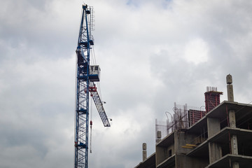 Construction crane above the building under construction against the sky with clouds