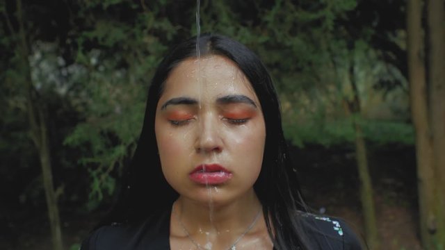 on the face of a beautiful brunette girl with makeup pours water from above. drops of water on the body of a girl. 4k. 4k video