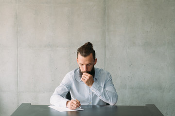 Corporate life and paperwork. Confused business man writing letter. Gray wall background. Copy...