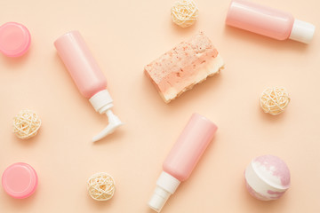 Spa therapy. Flat lay of handmade soap, cosmetic jars, lotion bottles and dispensers over peach color background.