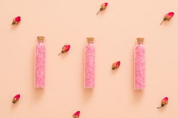 Rose essential oil diy bath salt in glass bottles. Floral pattern peach background.