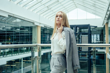 Fototapeta na wymiar Young elegant business woman in a stylish gray suit pants and jacket in a modern office with panoramic windows shopping center