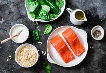 Ingredients for a balanced lunch - salmon fish, spinach, cream, orzo pasta on a dark background, top view