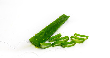 isolated on a white, sprinkled water background, a leaf of aloe, next to it slices with fresh aloe vera pulp