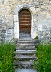 small wooden door in a thick and massive medieval city wall with steps leading through grass
