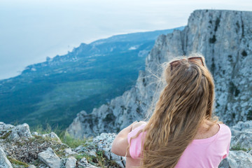 Naklejka premium girl with long blond hair sits on top of Mount Ai-Petri in Crimea with a sea view