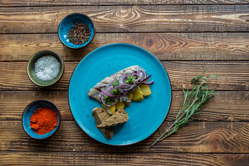 Fried potatoes and herring fish with onion on a wooden table.