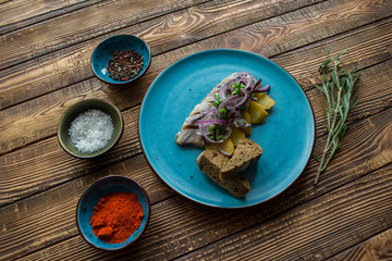 Fried potatoes and herring fish with onion on a wooden table.