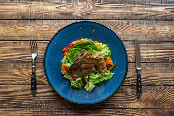 The salad with meat on the wooden table.