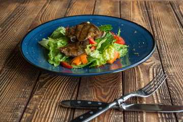 The salad with meat on the wooden table.