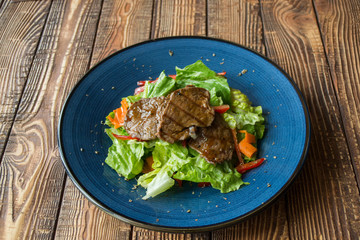 The salad with meat on the wooden table.