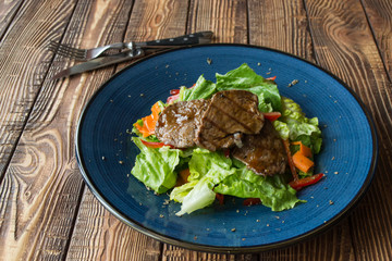 The salad with meat on the wooden table.