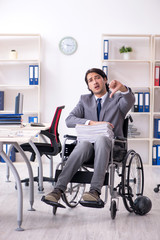 Young handsome employee in wheelchair working in the office  