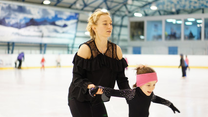 Female coach in figure skating training little girl at indoor rink