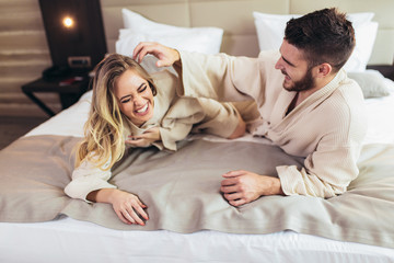 Young loving couple in bathrobes relaxing on bed at hotel