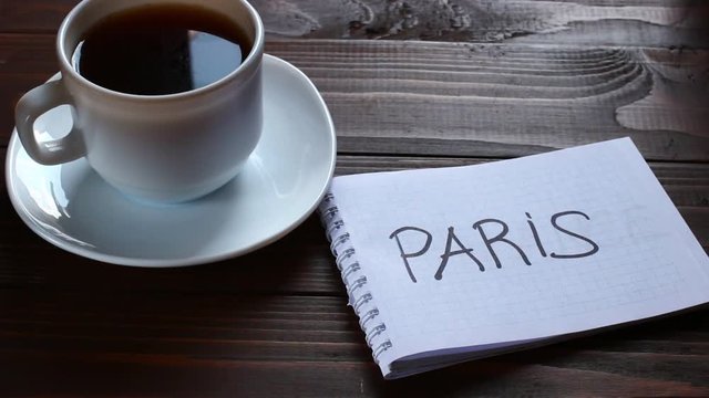 Paris inscription and word in a notebook near a cup of coffee