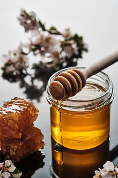 A jar of honey with honeycombs and a stick on a light background.