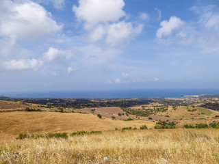 Fototapeta premium An idyllic view of a hilly fields in Cyprus. Slopes are overgrown with grains and small bushes. In the back some smaller mountains are visible. Great overcast, spreading all over the sky.