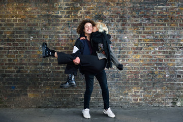 Fototapeta na wymiar Man holding his girlfriend in his arms in front of a brick wall typical of London