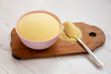 Dry semolina durum flour in a pink bowl over white wooden surface, side view. Close-up.
