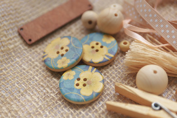 Close-up: Wooden buttons with blue floral print and wooden clothespins with wooden beads for needlework lie on the burlap
