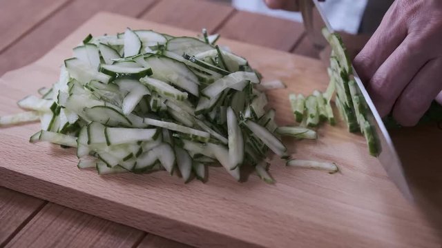 cook slices cucumbers on a cutting board, close-up slicing cucumbers