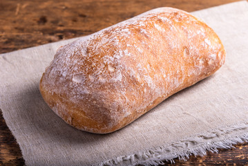 Traditional Italian ciabatta bread on a linen napkin on an old rustic wooden table, close-up, top view