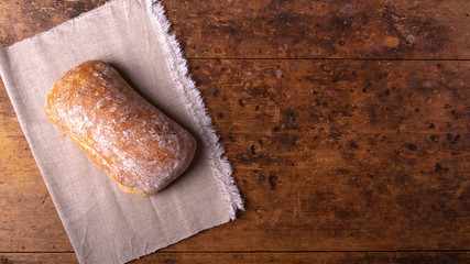 Traditional Italian ciabatta bread on a linen napkin on an old rustic wooden table, copy space, top view