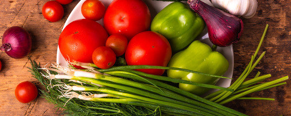 Fresh  tomatoes, cherry, green peppers, chili peppers, onions, cucumbers, garlic and herbs in a plate on a rustic wooden table - panoramic culinary background, rural style, healthy eating concept