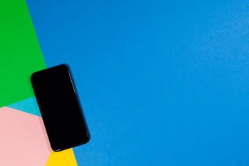 A black phone is laying on a flat surface of green, blue, pink, and yellow
